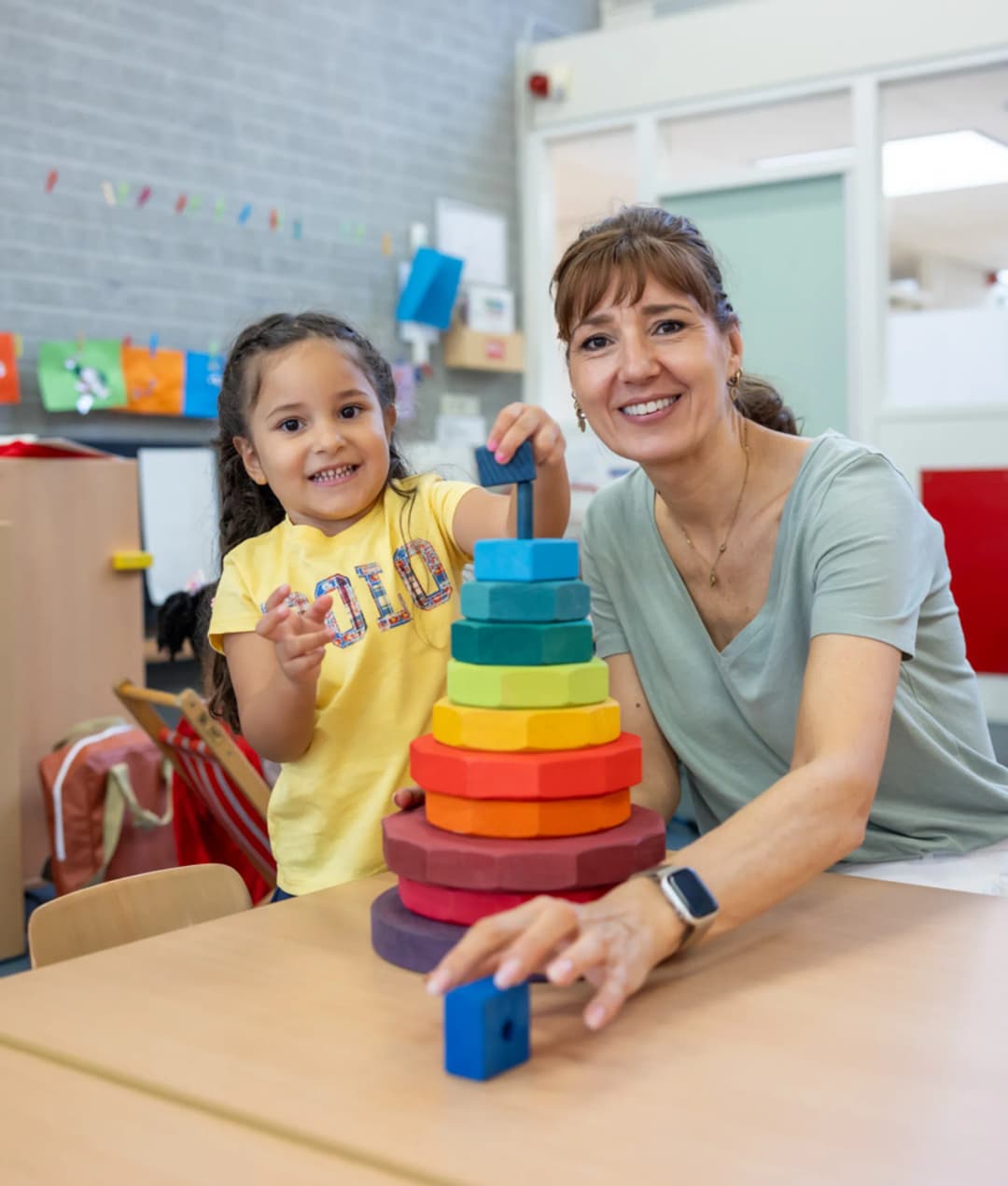 Kind stapelt houten ringen samen met pedagogisch medewerker bij kinderopvang Kind&co ludens