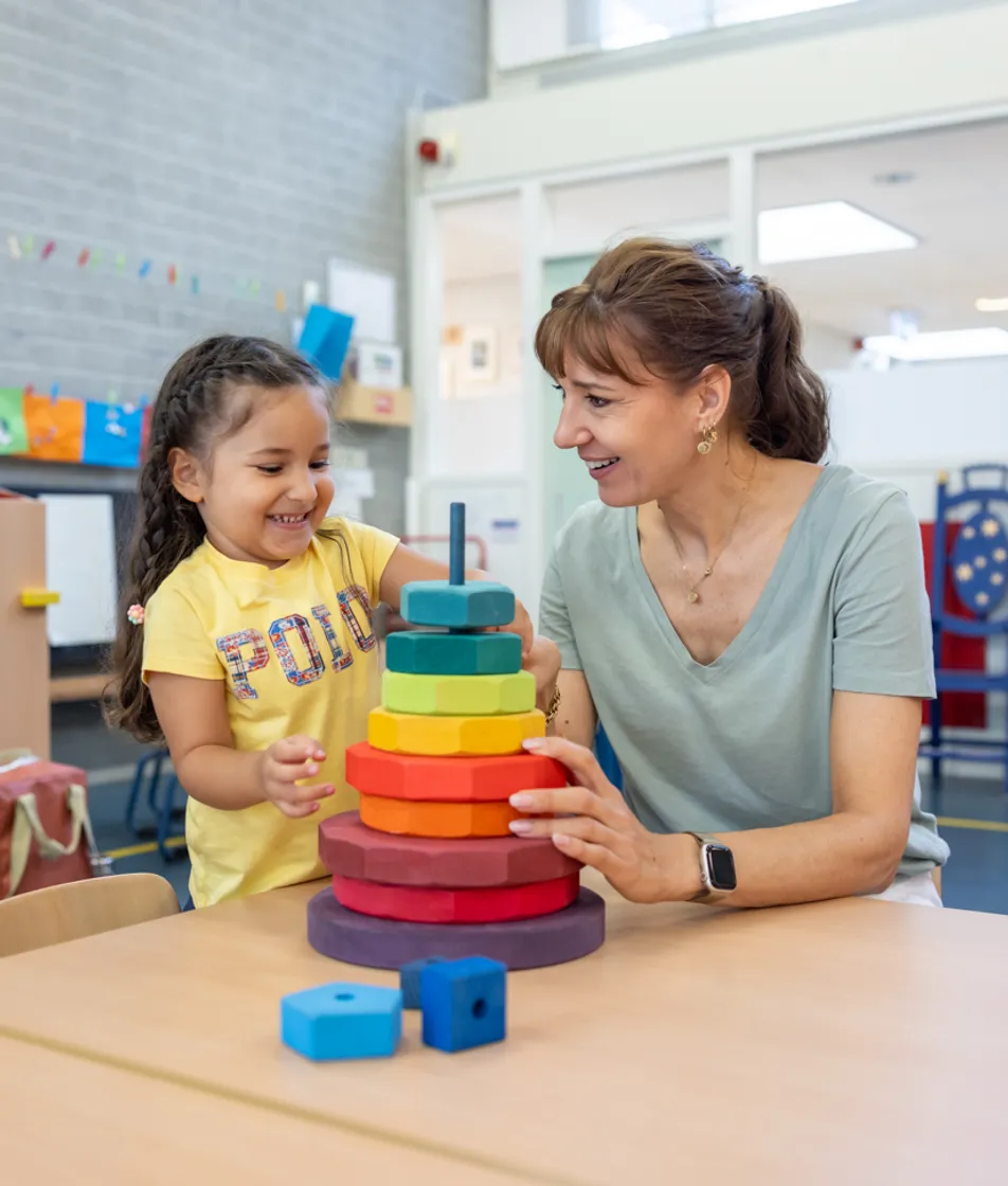Kind stapelt houten ringen samen met pedagogisch medewerker bij kinderopvang Kind&co ludens